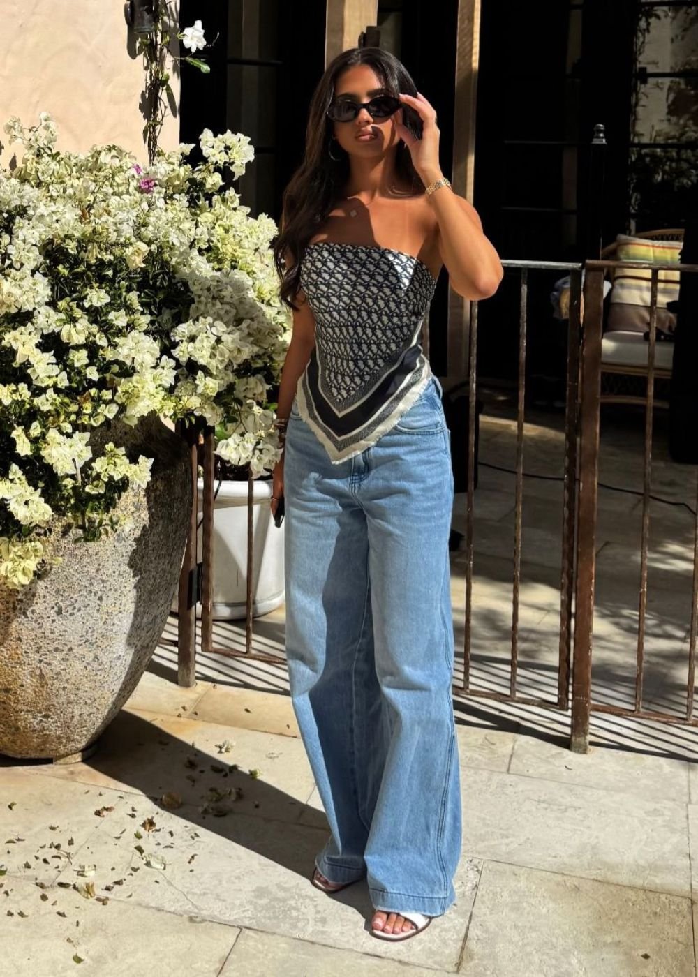 Mulher mostrando como usar lenço como blusa. Look composto por lenço em preto e branco, calça jeans e óculos de sol.