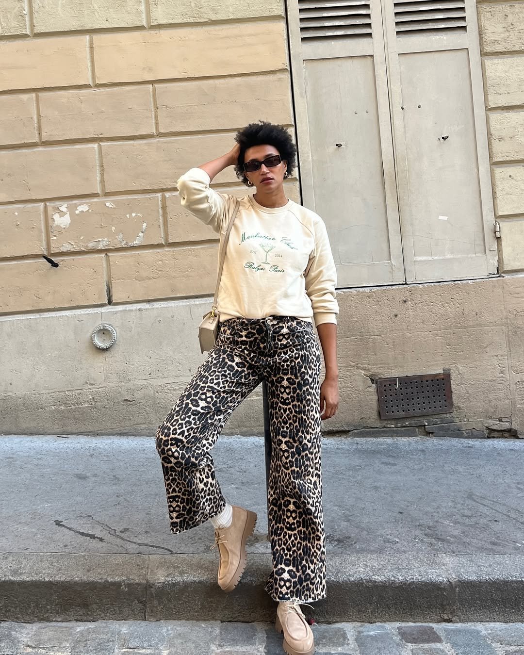 Pessoa com calça de estampa animal, suéter claro e óculos de sol, em pose descontraída com look de festival.