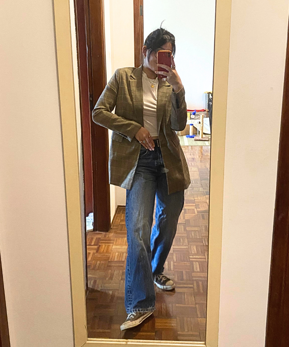Pessoa usando blazer xadrez, camiseta branca e jeans flare, combinados com tênis casual no espelho.