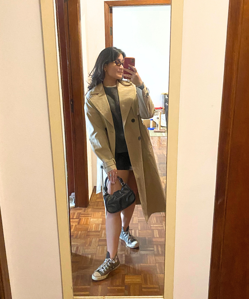 Pessoa usa trench coat bege com tênis estilo Converse e bolsa pequena, posando frente ao espelho. Dicas de como usar all star em 2025.