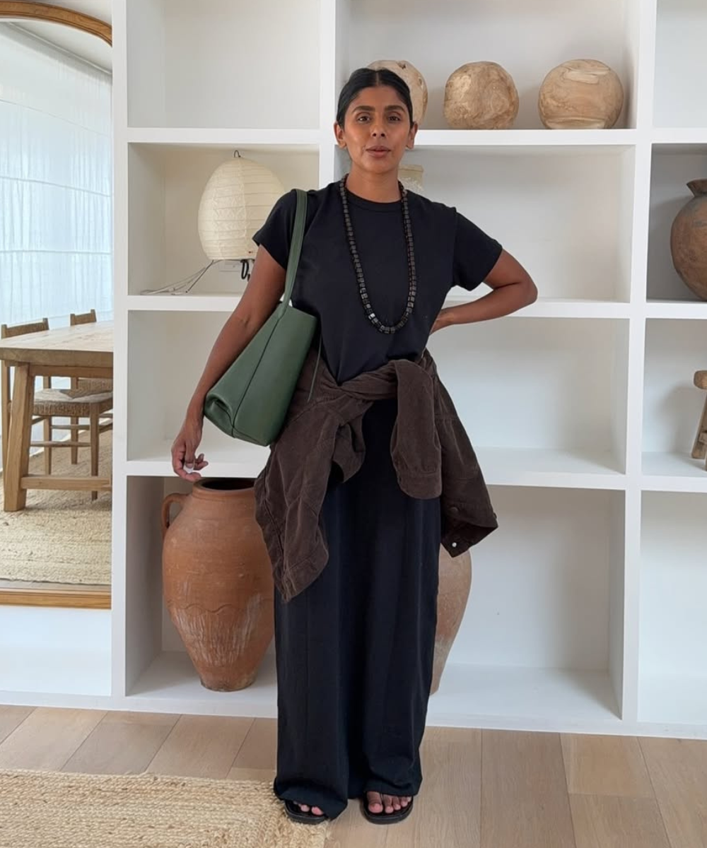 Pessoa de roupa preta com sandália flat e bolsa verde em ambiente decorado.