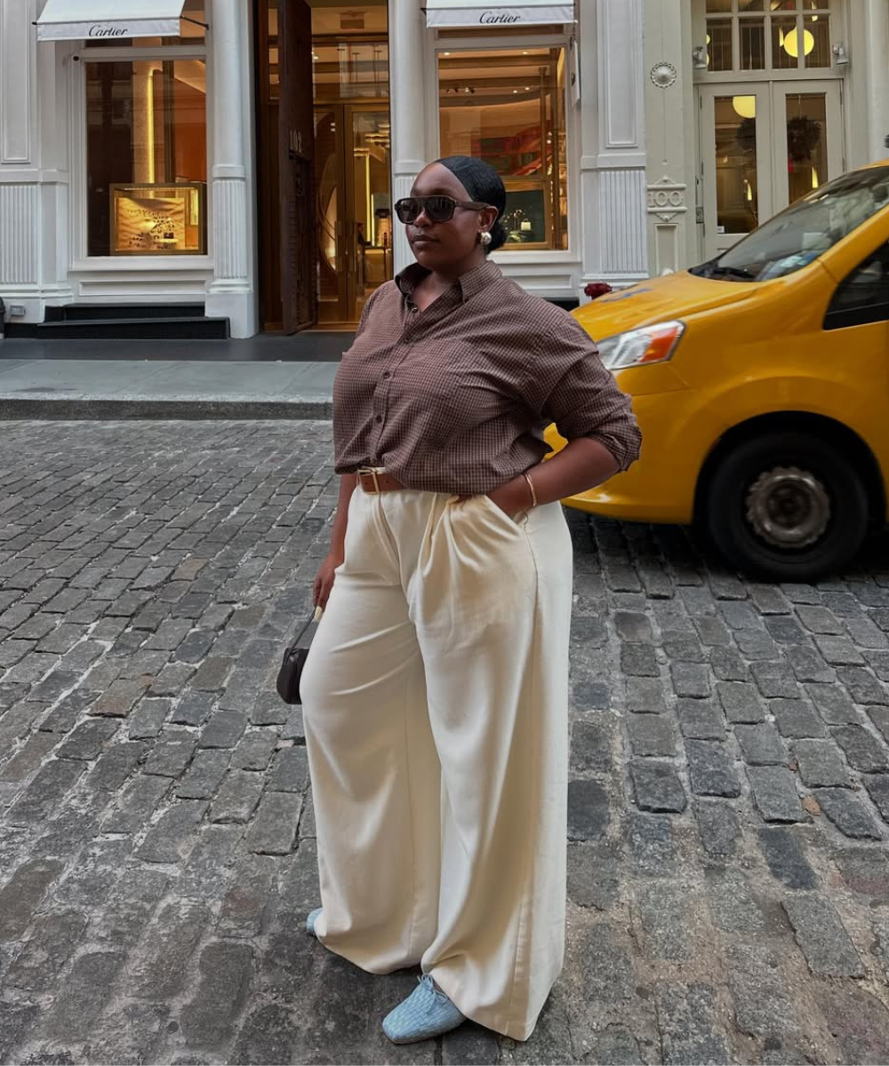 Mulher em calças brancas largas e camisa marrom, estilo casual, em rua com táxi amarelo. Inspiração de looks confortáveis com calça.