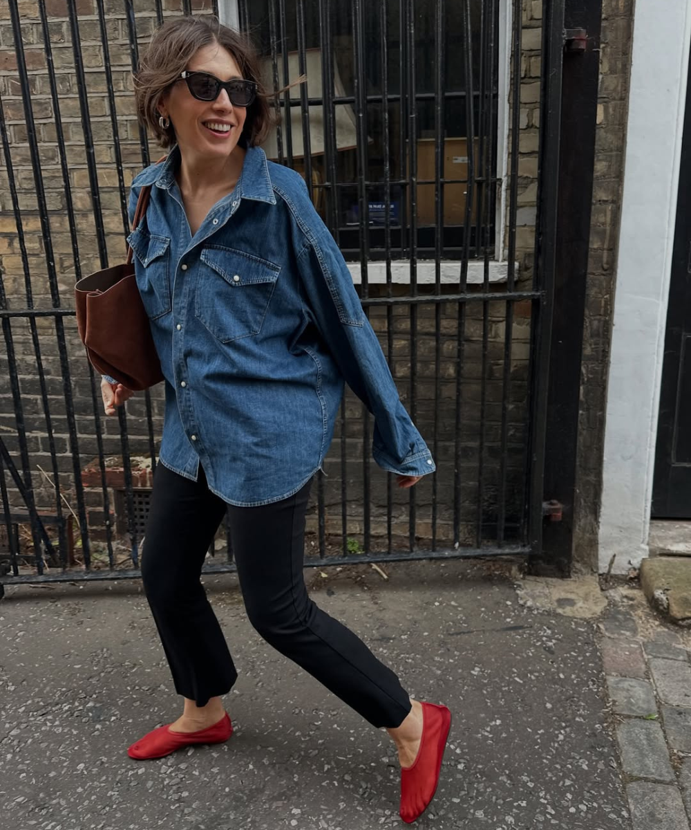 Pessoa caminhando e sorrindo com calça preta, camisa jeans e sapatilhas vermelhas, mostrando estilo casual e confortável.