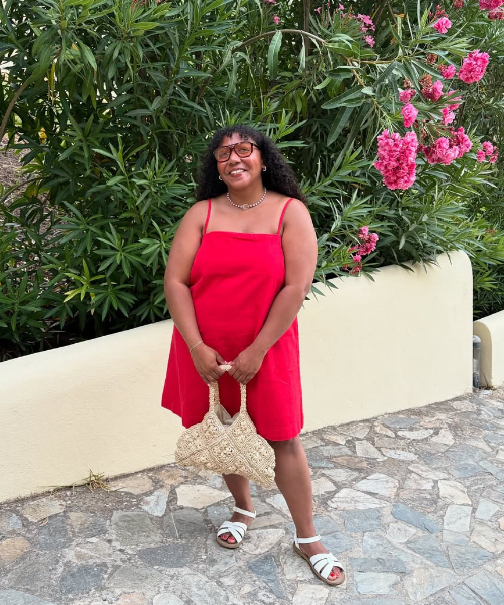 Vestido vermelho e rasteirinha branca compõem look bonito com bolsa de palha, ao lado de flores.