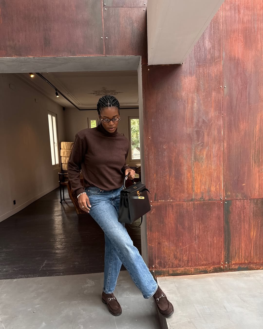 Pessoa com suéter marrom e jeans, segurando uma bolsa preta. Um dos looks femininos estilosos.