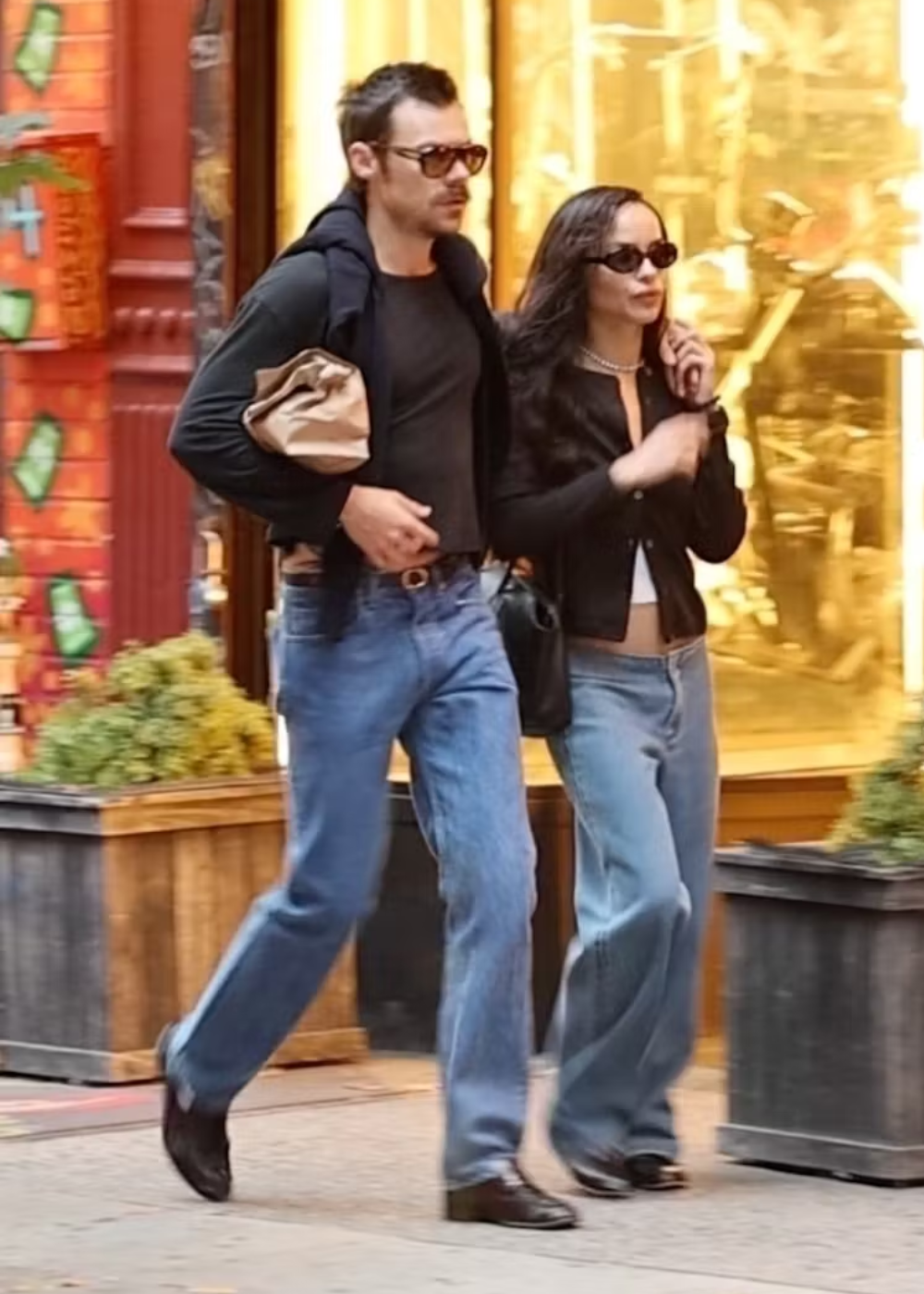 Um homem e uma mulher caminhando juntos, ambos usando jeans e óculos escuros.
