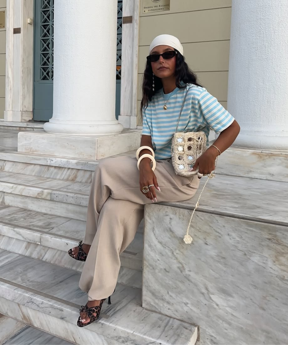 Pessoa com blusa listrada e calça bege, usando óculos escuros e acessórios, exemplifica looks tendência para primavera.