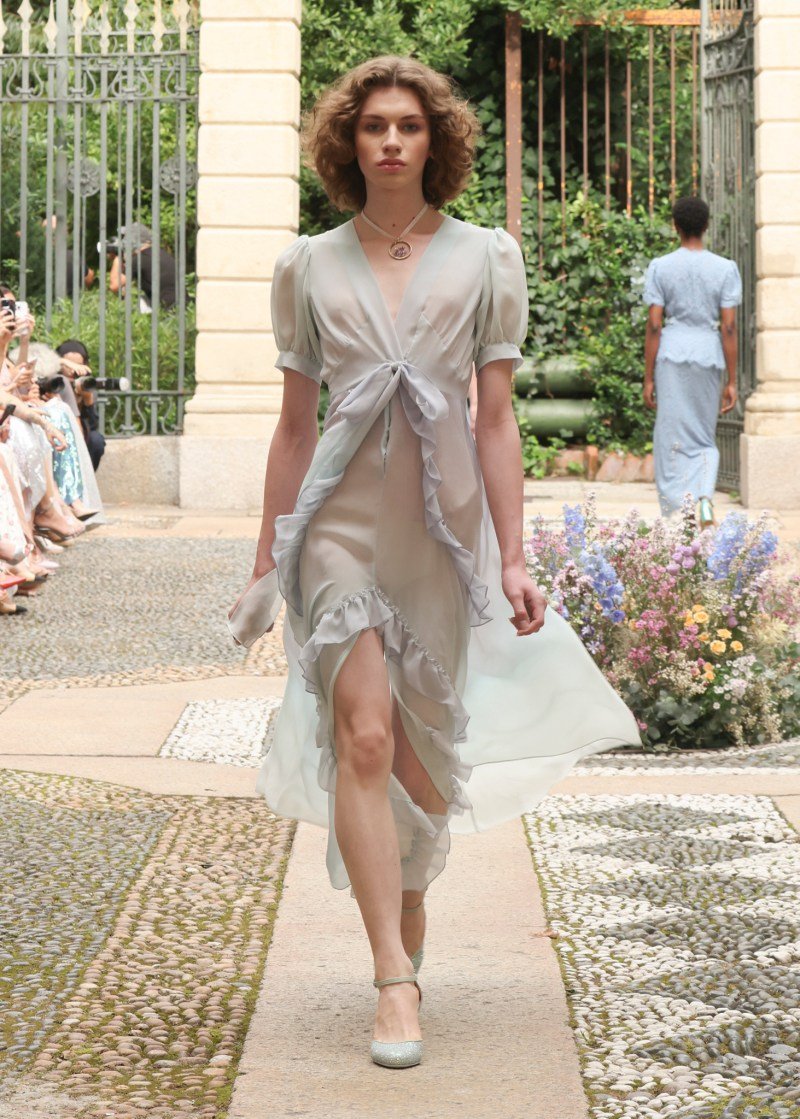 Modelo com vestido fluido esverdeado desfila na Milan Fashion Week SS26, em passarela ao ar livre.