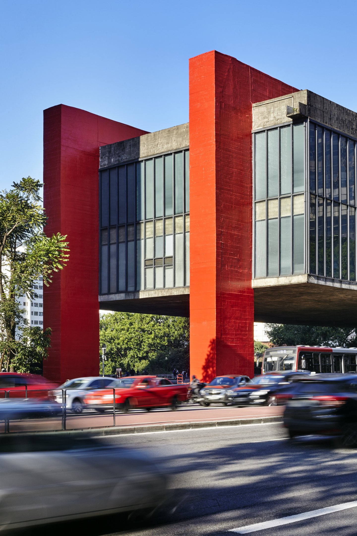 Edifício suspenso de concreto e vidro do MASP com colunas vermelhas e tráfego de carros na avenida.