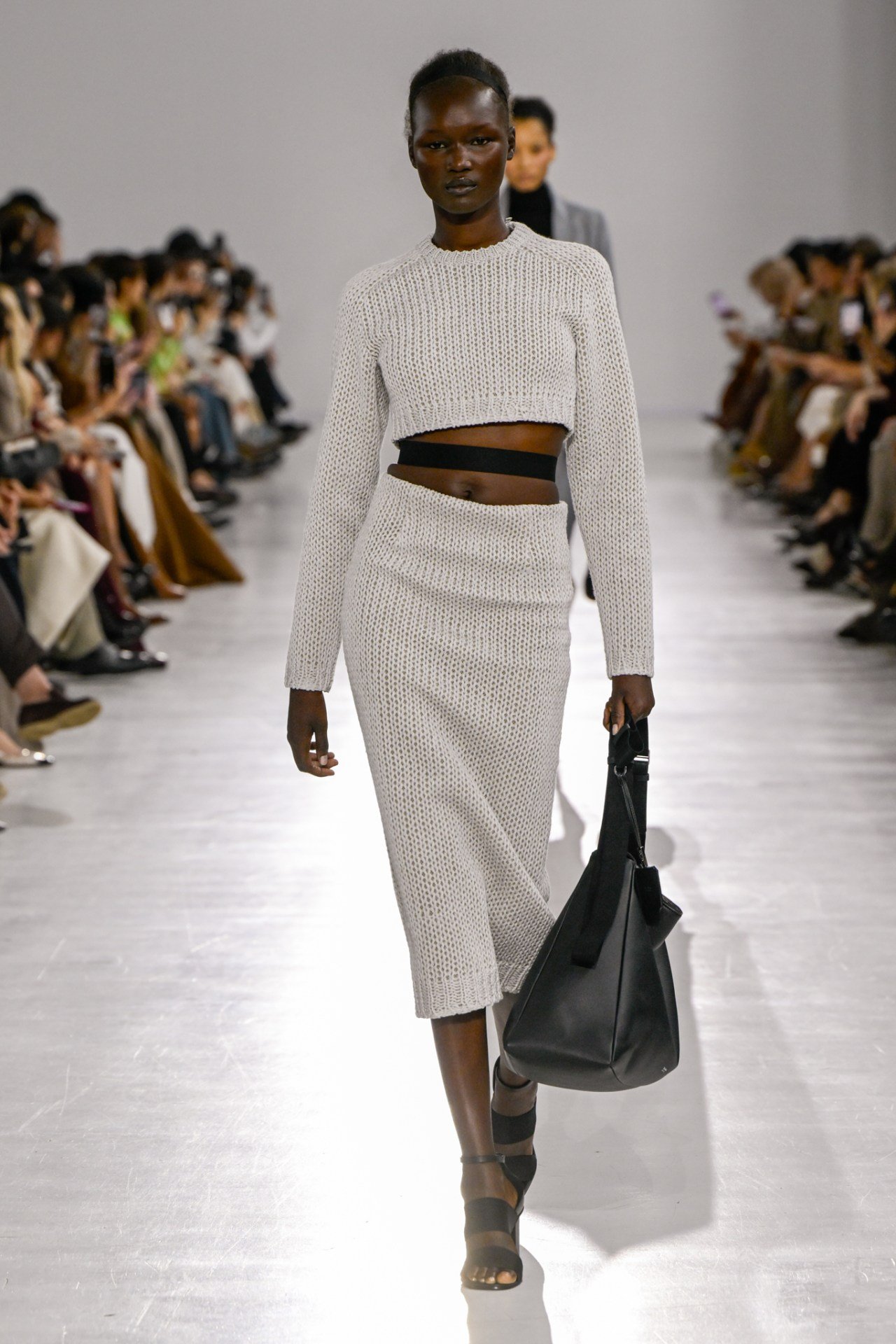 Modelo em passarela com conjunto de tricô cinza e bolsa preta, Milan Fashion Week SS26.