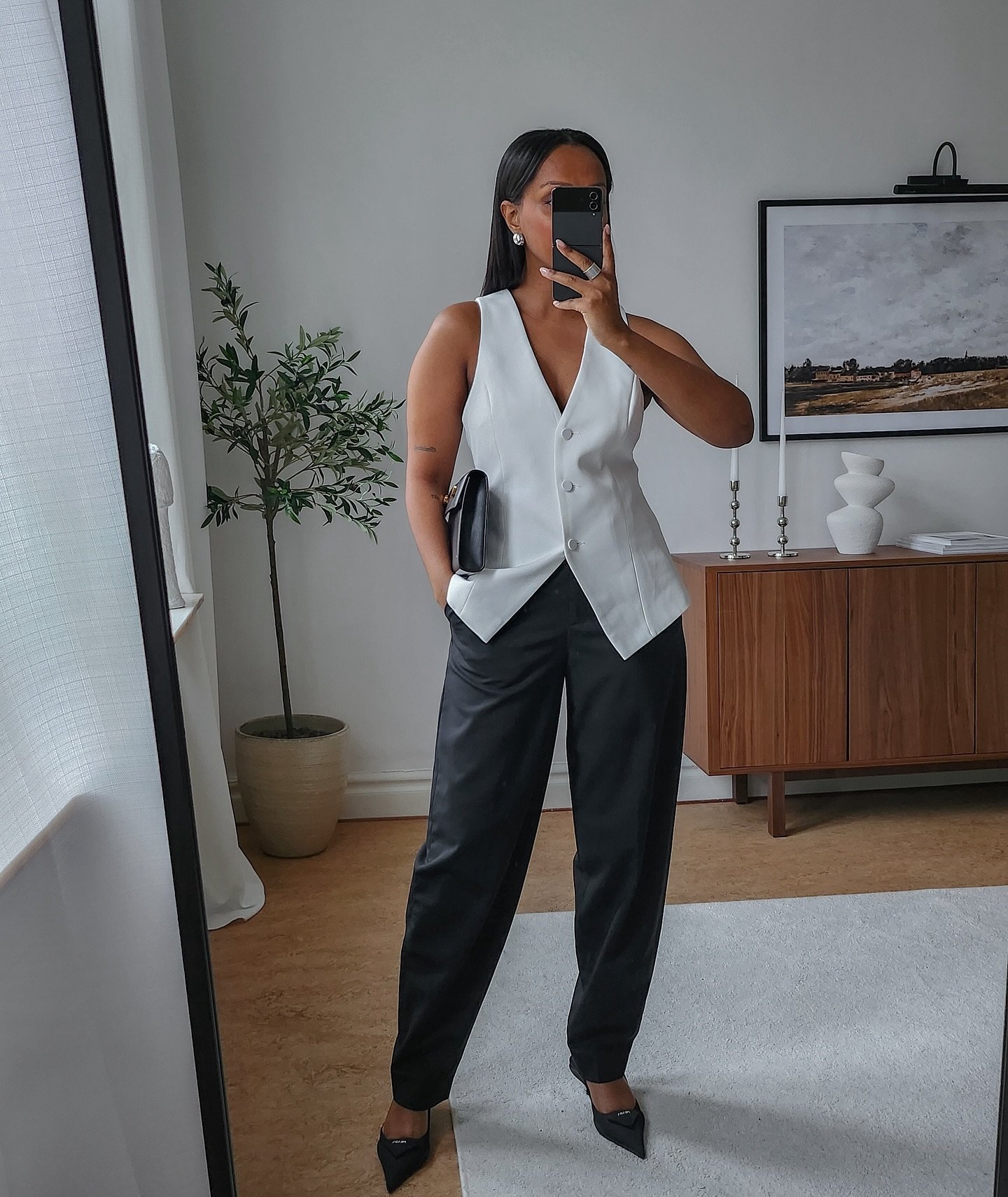 Mulher em look de trabalho elegante com colete branco e calça preta em ambiente moderno.