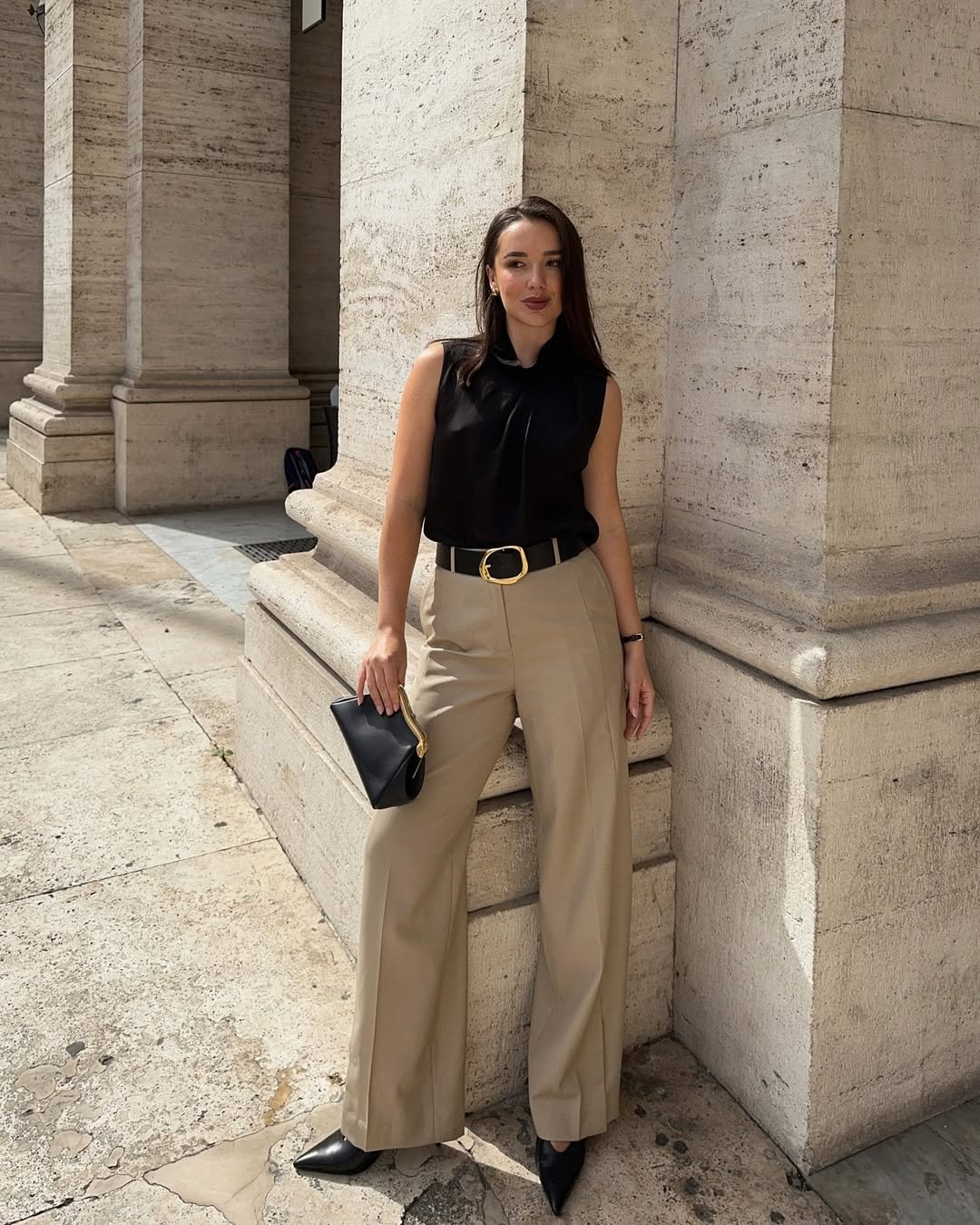 Mulher usando blusa preta sem mangas e calça bege, ideal para um elegante look profissional.