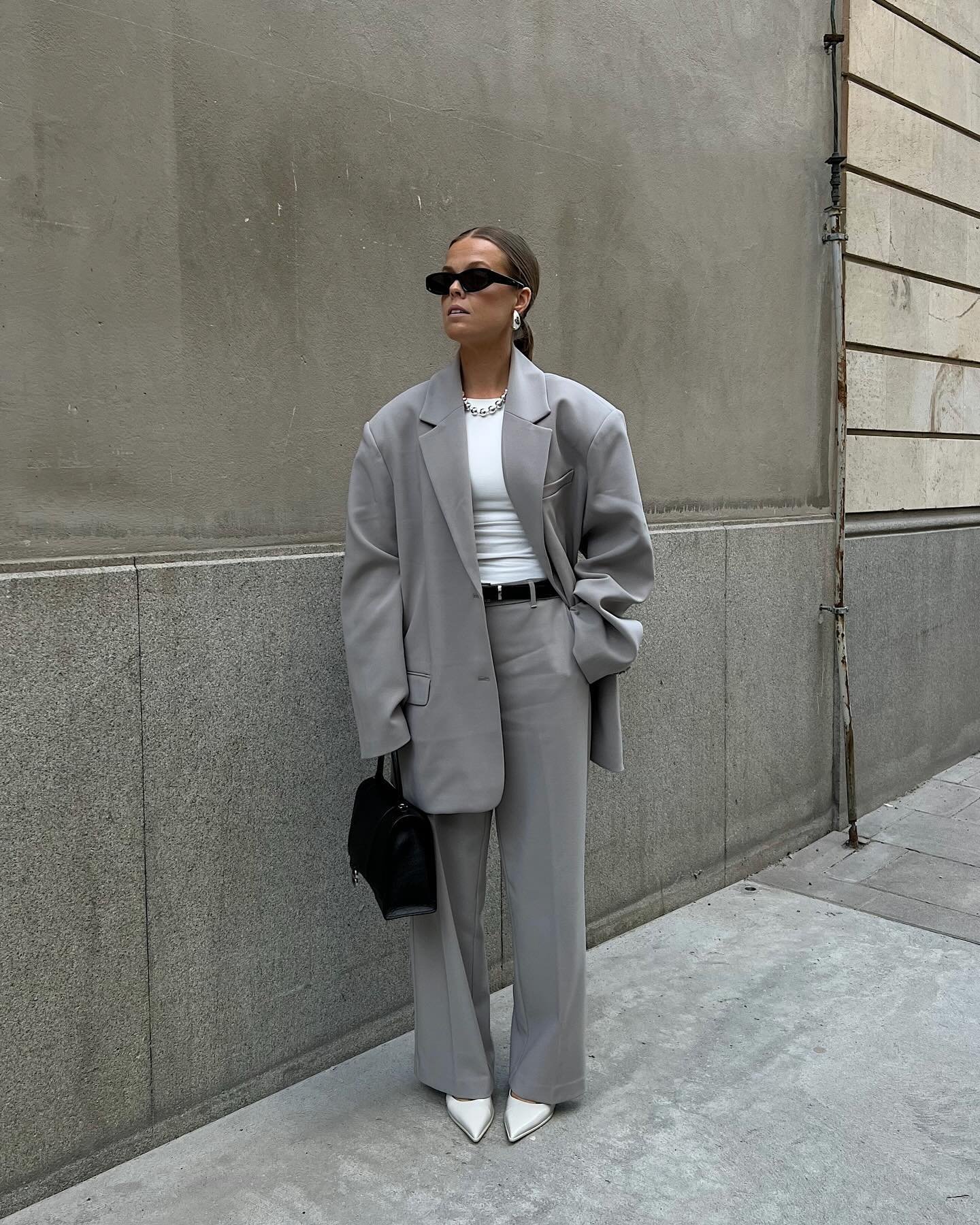 Pessoa usando terno cinza elegante, com blusa branca e óculos escuros, representando um dos melhores looks de trabalho.