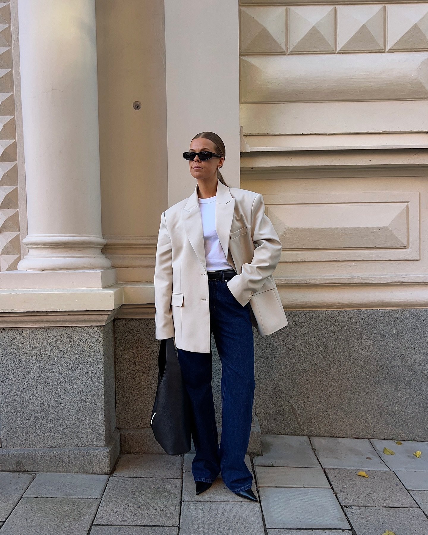 Blazer bege, camiseta branca e jeans azul com acessórios pretos compõem um dos melhores looks de trabalho.