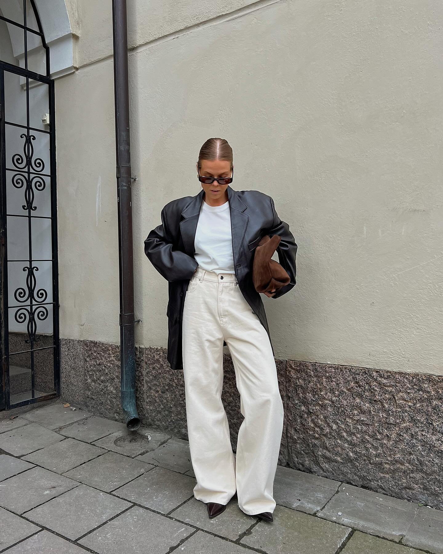 Blazer de couro preto sobre camiseta branca e calça ampla creme, destacando tendências em melhores looks de trabalho.