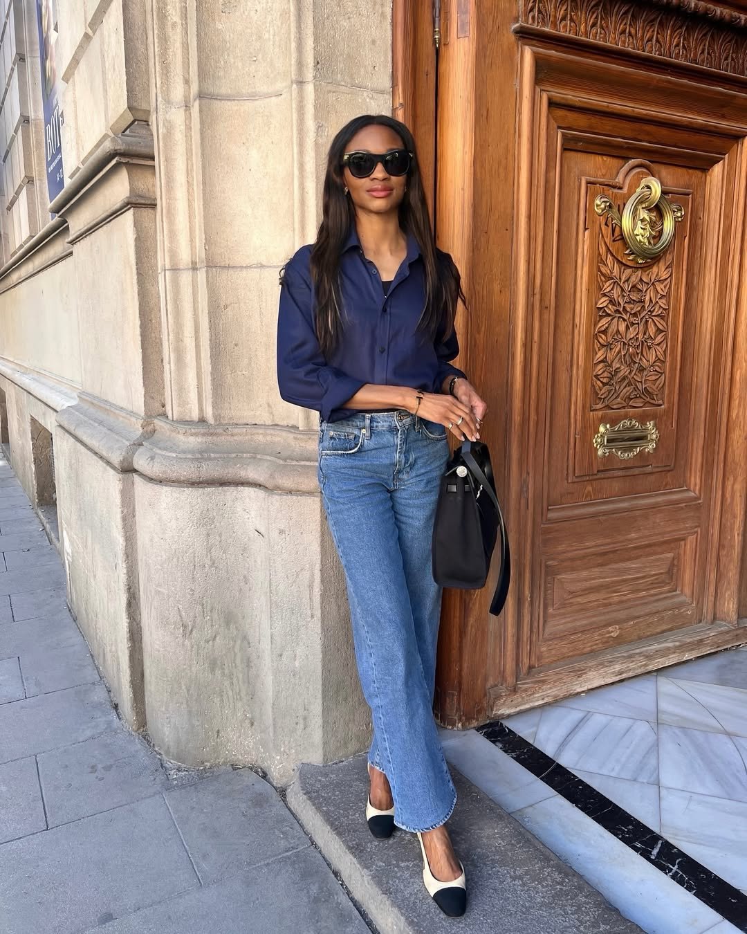 Pessoa com camisa azul e jeans, encostada em porta de madeira, exemplificando um dos melhores looks de trabalho.