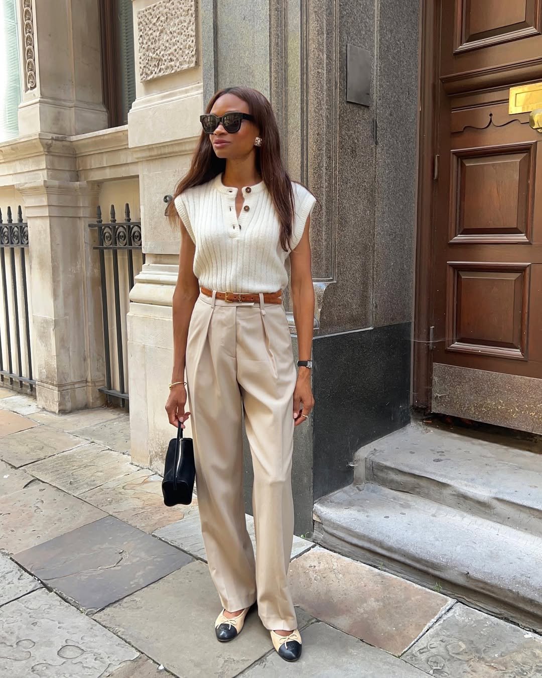 Sofisticação no look de trabalho: calça bege, blusa branca sem mangas, acessórios clássicos e bolsa preta.