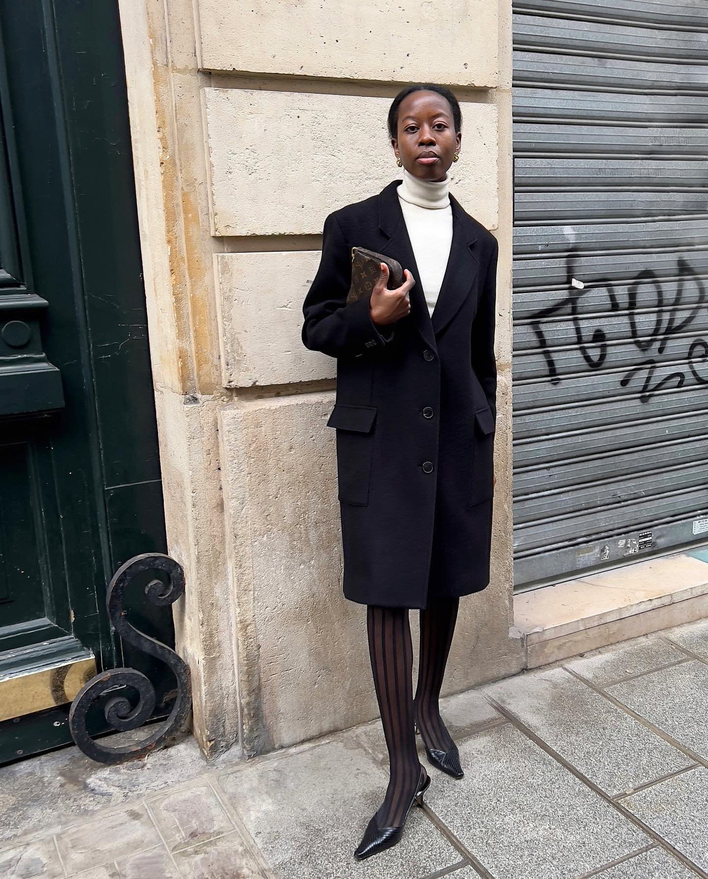Parece um outfit para trabalho: casaco preto elegante, gola alta clara, meia-calça listrada, sapatos de salto.