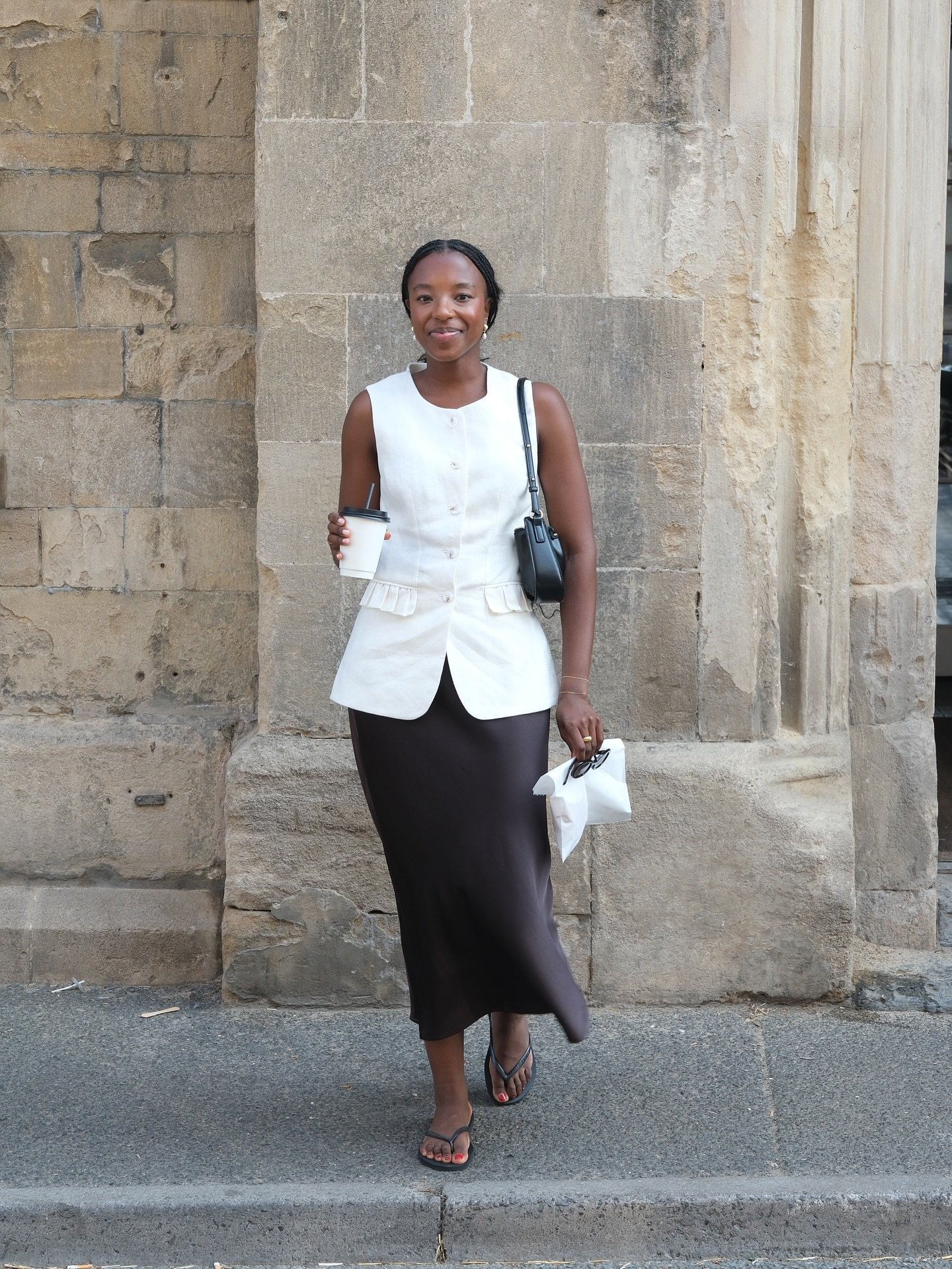 Pessoa em look casual, segurando café em um ambiente urbano. Use de tons neutros e cortes elegantes ilumina um dos melhores looks de trabalho.