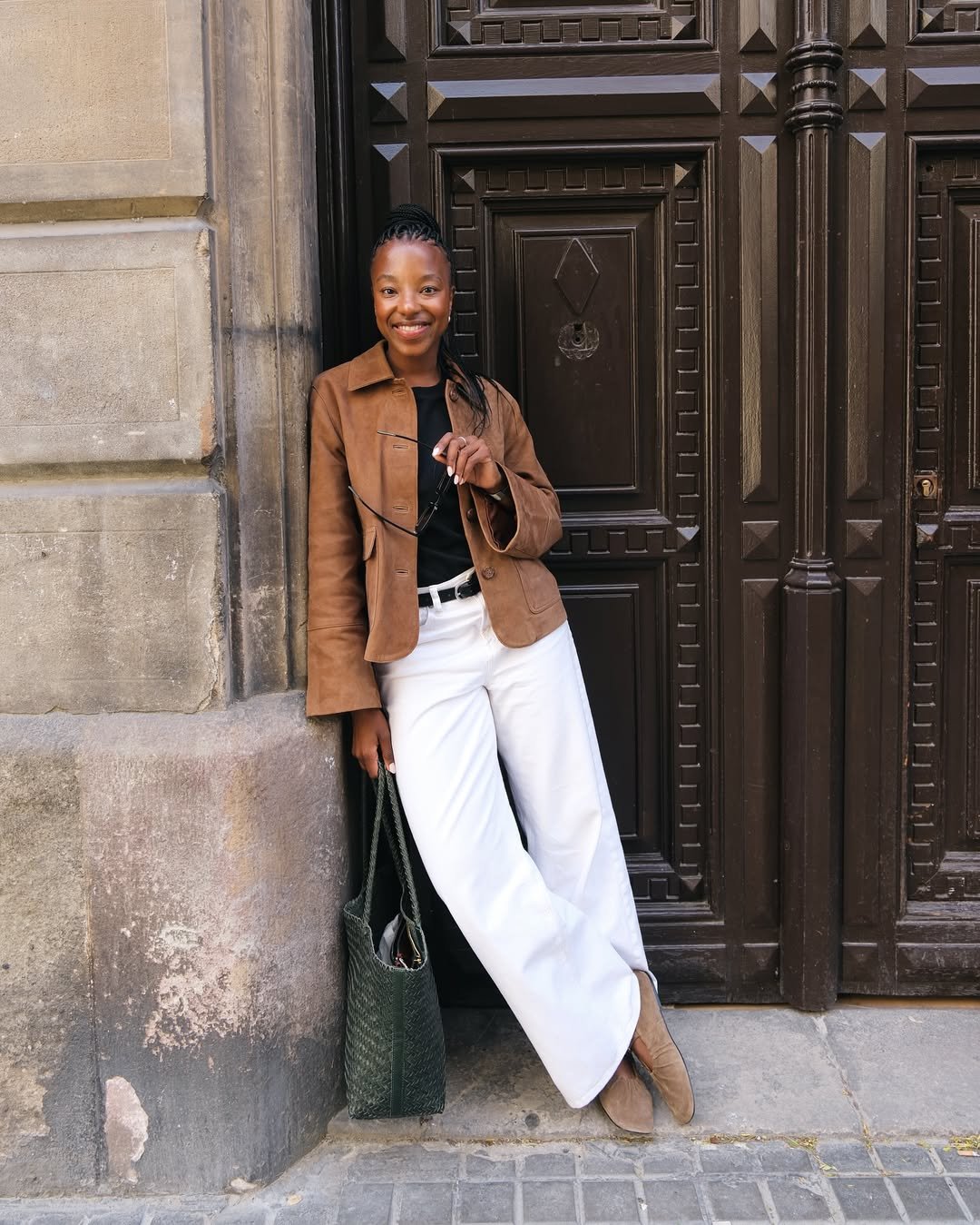Pessoa com blazer marrom e calça branca apoiada em uma parede, esbanjando elegância dos melhores looks de trabalho.
