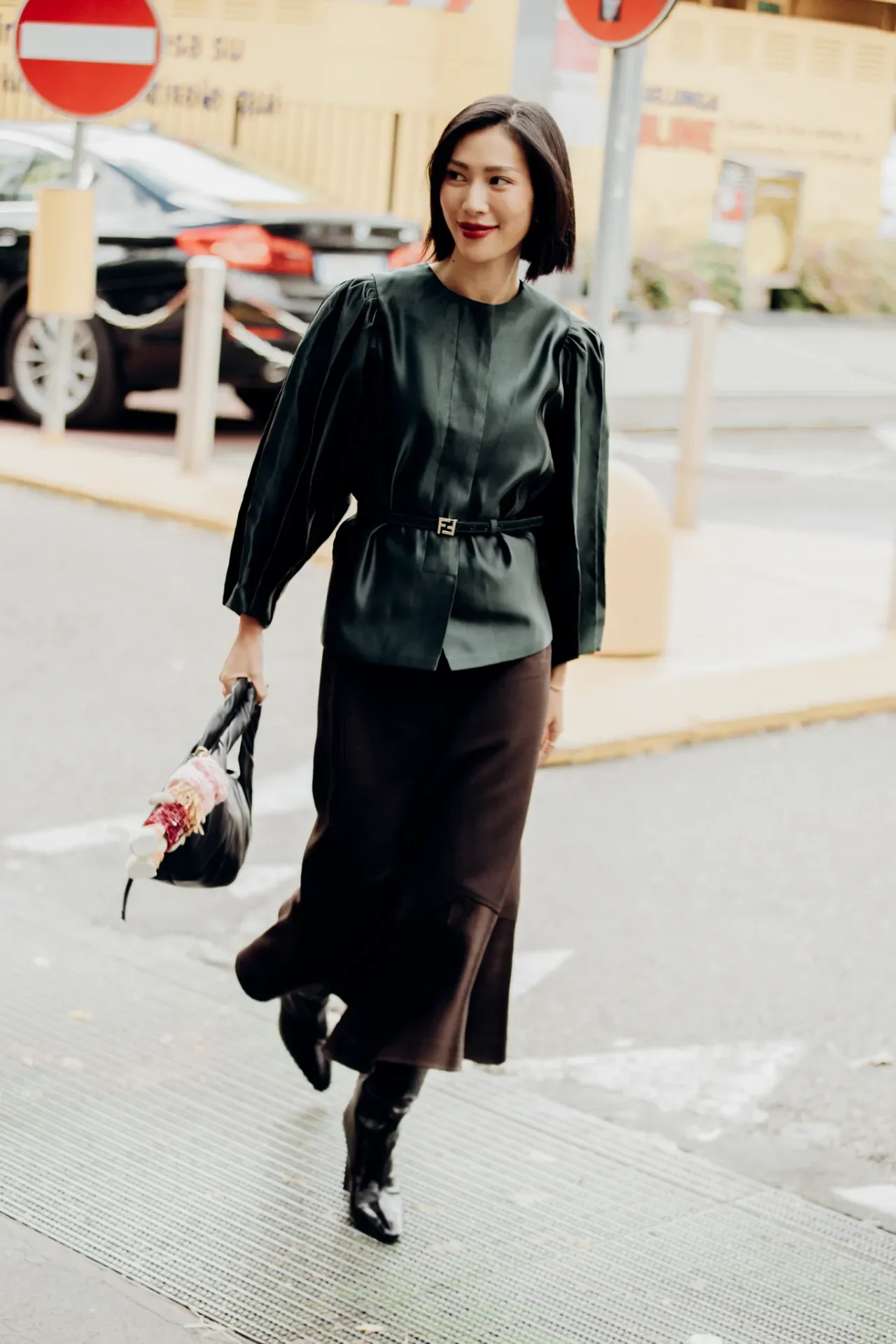 Mulher caminhando em rua, vestindo blusa escura elegante e saia longa, segurando bolsa. Exemplo de truques de estilo fáceis.