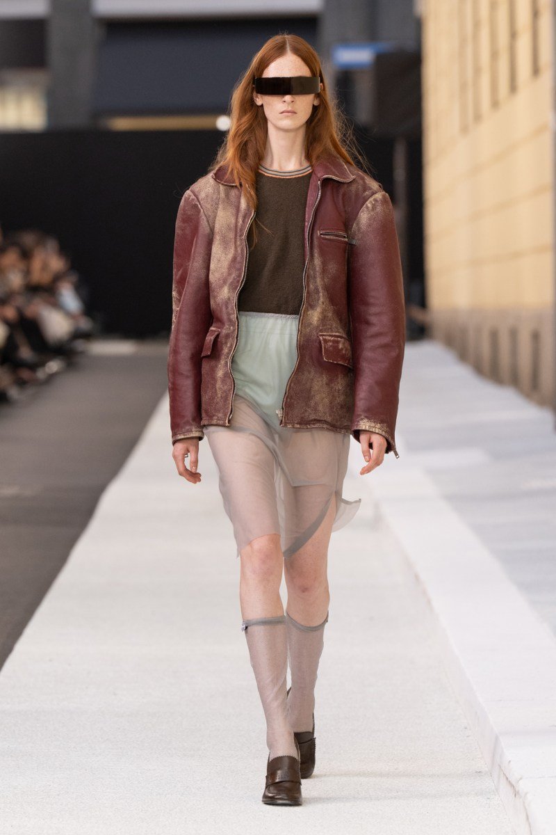 Modelo com jaqueta de couro e saia transparente em desfile da Milan Fashion Week SS26.