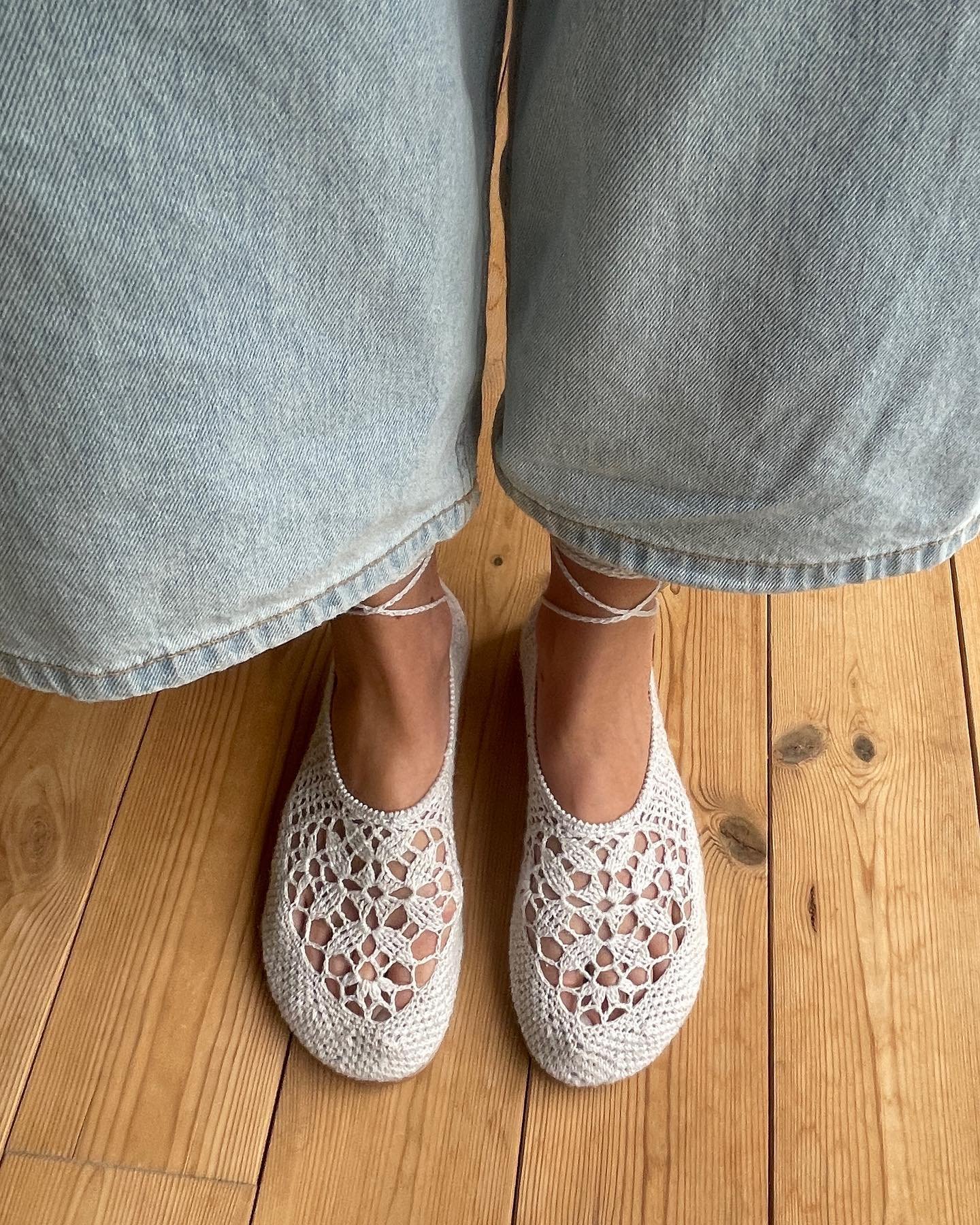 Calçado boho de crochê bege em pés com calça jeans, sobre piso de madeira.