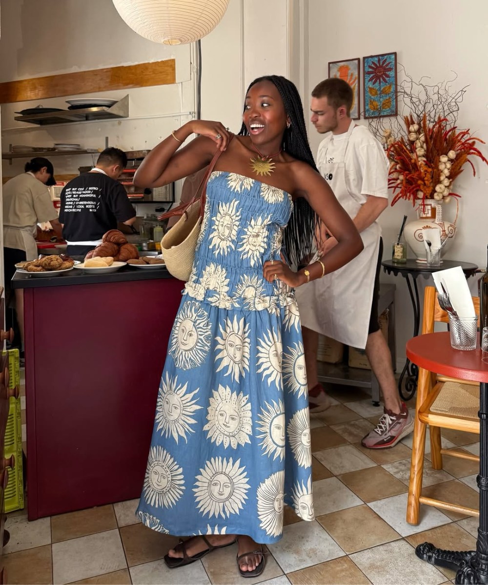 Mulher feliz em vestido azul estampado com desenhos de sol, em ambiente de padaria. Usa um dos modelos de vestidos de primavera.