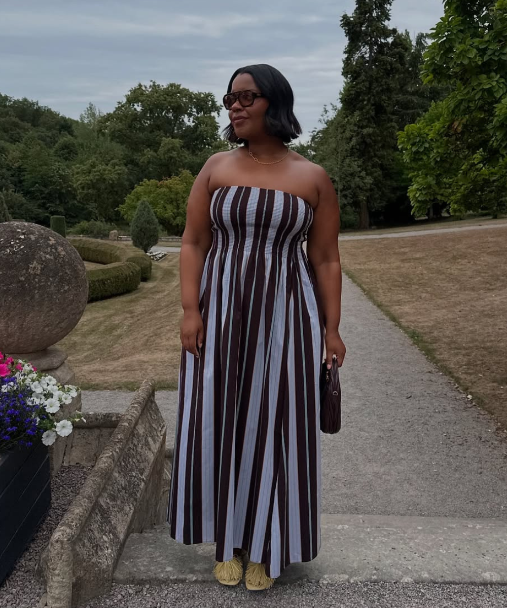 Vestido listrado em tons de marrom e azul, usado numa paisagem verdejante com flores, evocando a primavera.