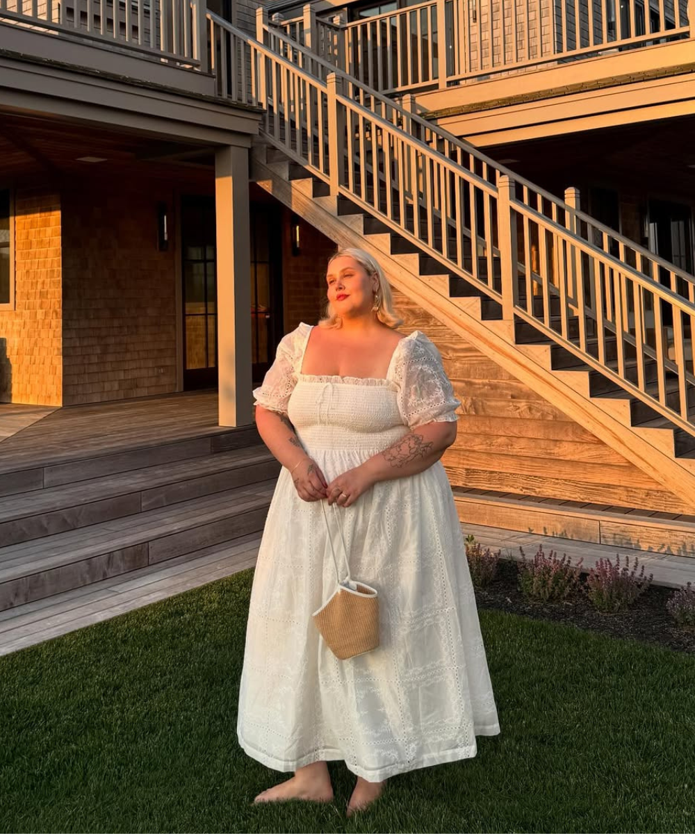 Mulher de vestido de primavera branco em um jardim ao entardecer, perto de escadas de madeira.