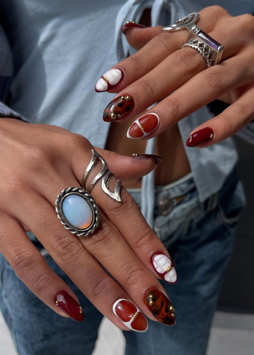 Unhas decoradas com esmalte vermelho e detalhes dourados e brancos, exibindo a tendência das cores de esmalte do verão 2026.