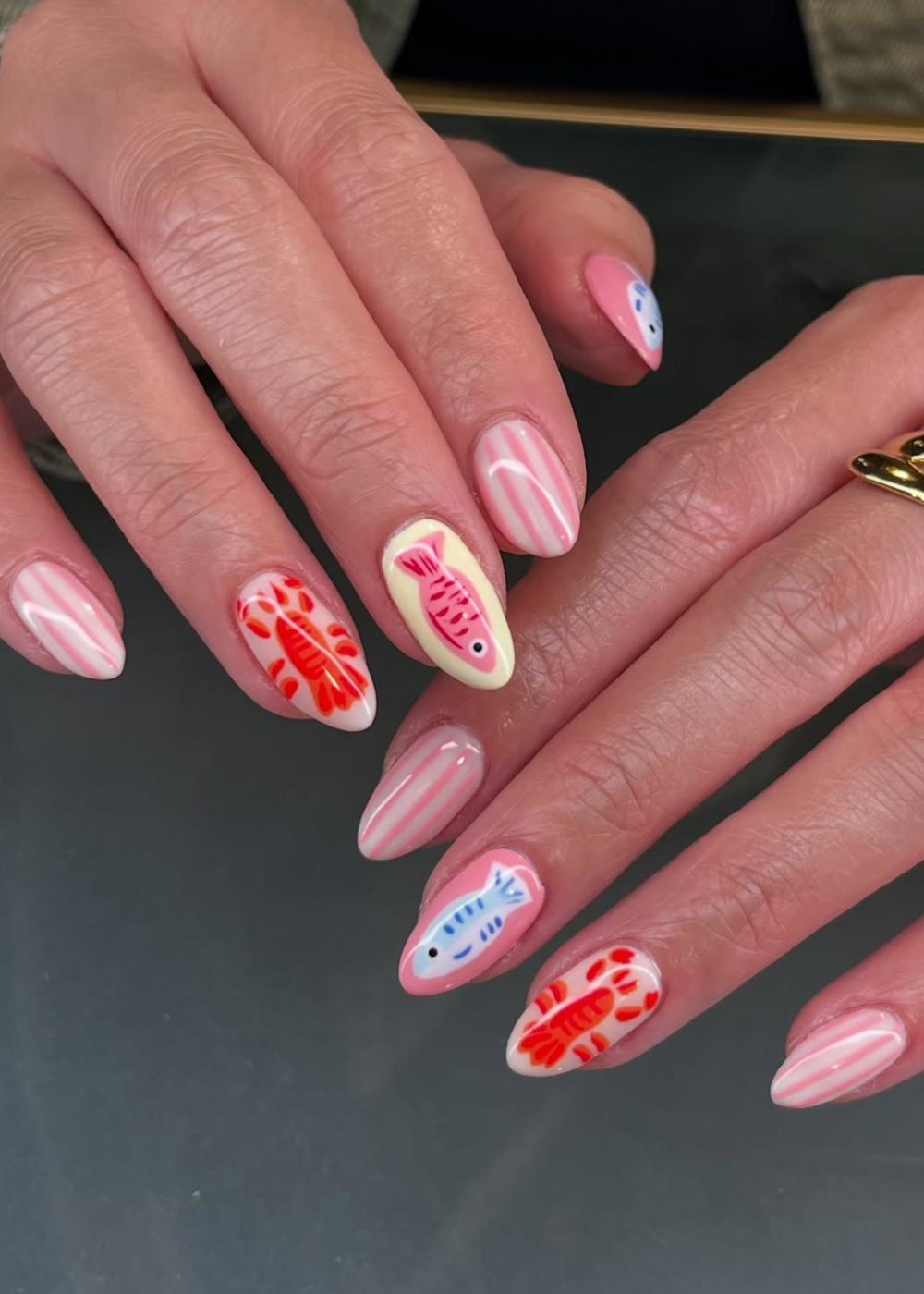 Unhas decoradas com desenhos coloridos de peixes e lagostas, representando nail arts tendência do verão 2026.