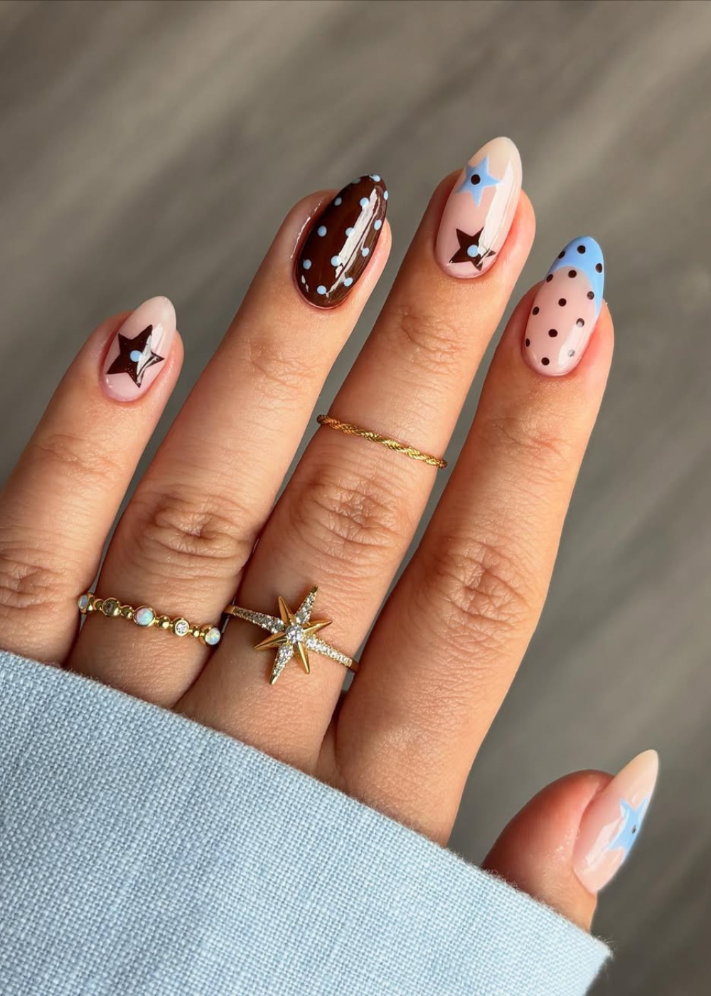 Unhas decoradas com estrelas e bolinhas em tons pastel e marrons, exibindo a tendência nail arts do verão 2026.