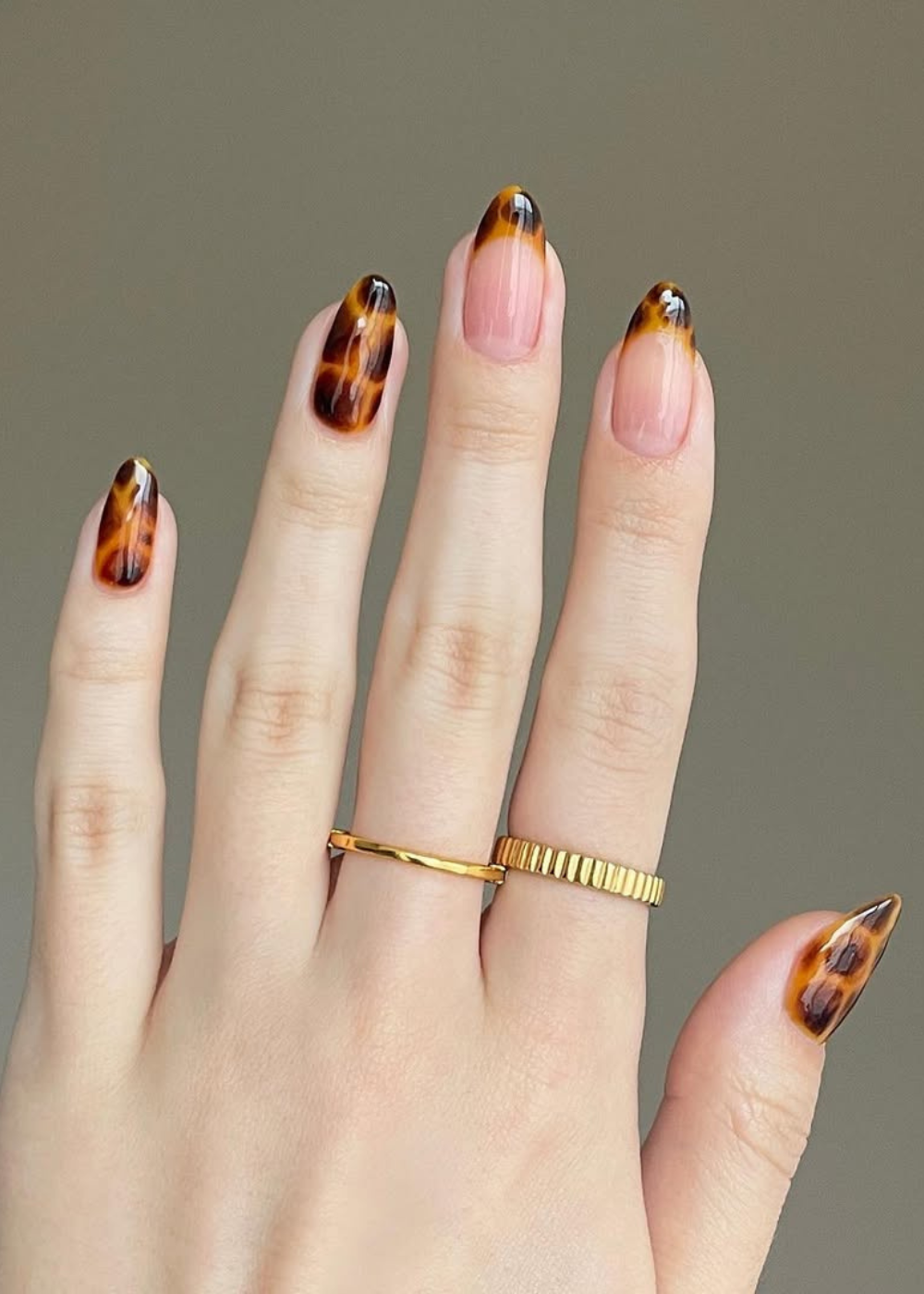 Unhas com estampa tartaruga, tendência do verão 2026, usando joias douradas.