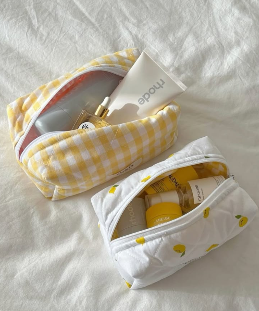 Duas nécessaires contendo produtos de beleza sobre um tecido branco, uma xadrez amarela e outra branca com motivos de limão.
