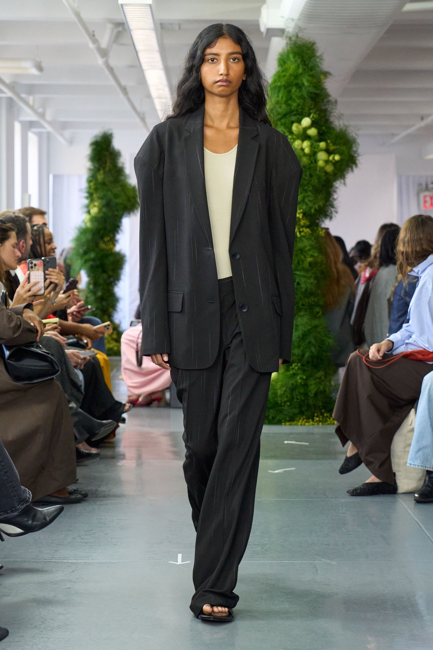 Modelo em look elegante da New York Fashion Week SS26, vestindo blazer preto e calça.plateia observa.