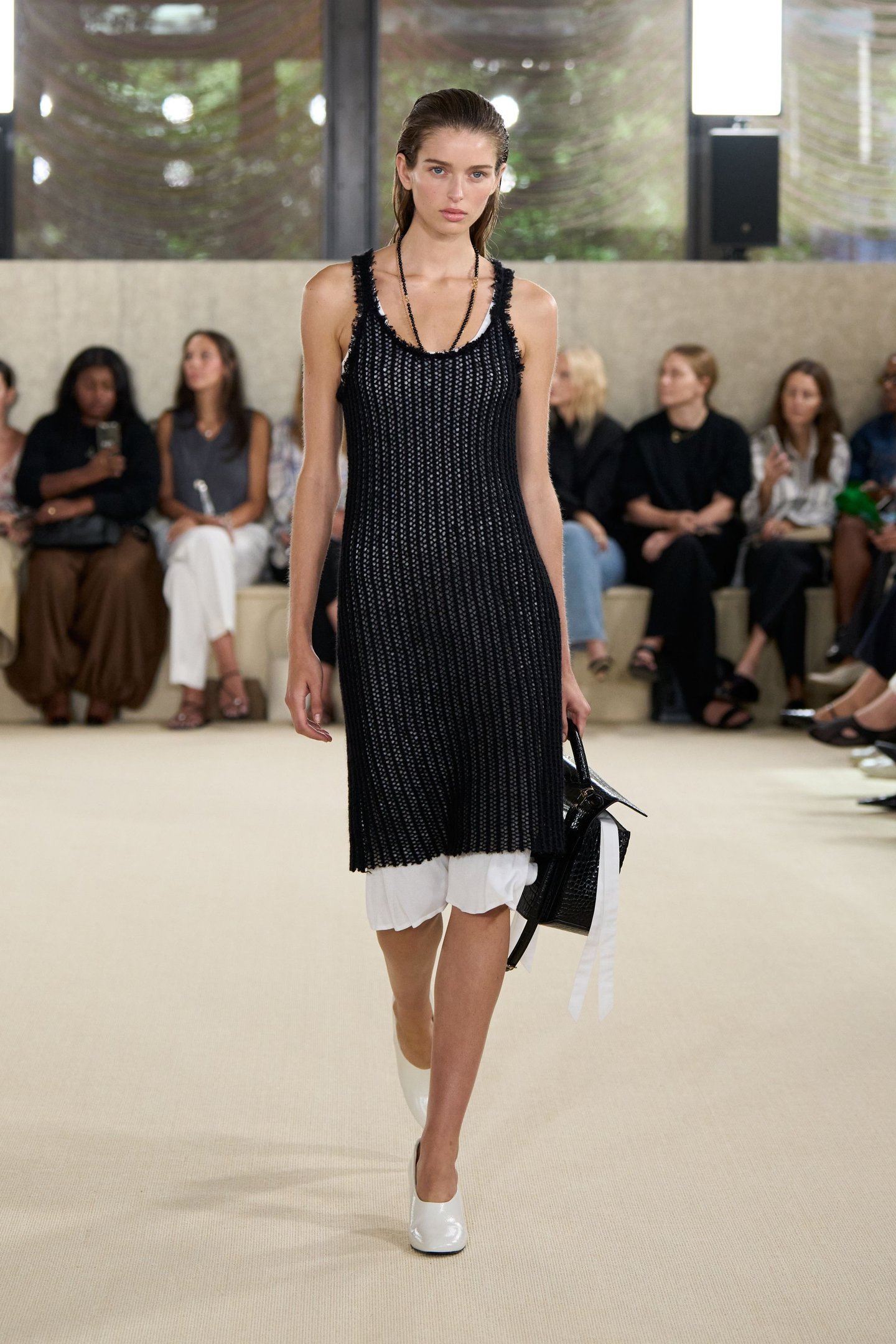 Modelo desfilando em vestido preto e branco durante o New York Fashion Week SS26. Plateia ao fundo.