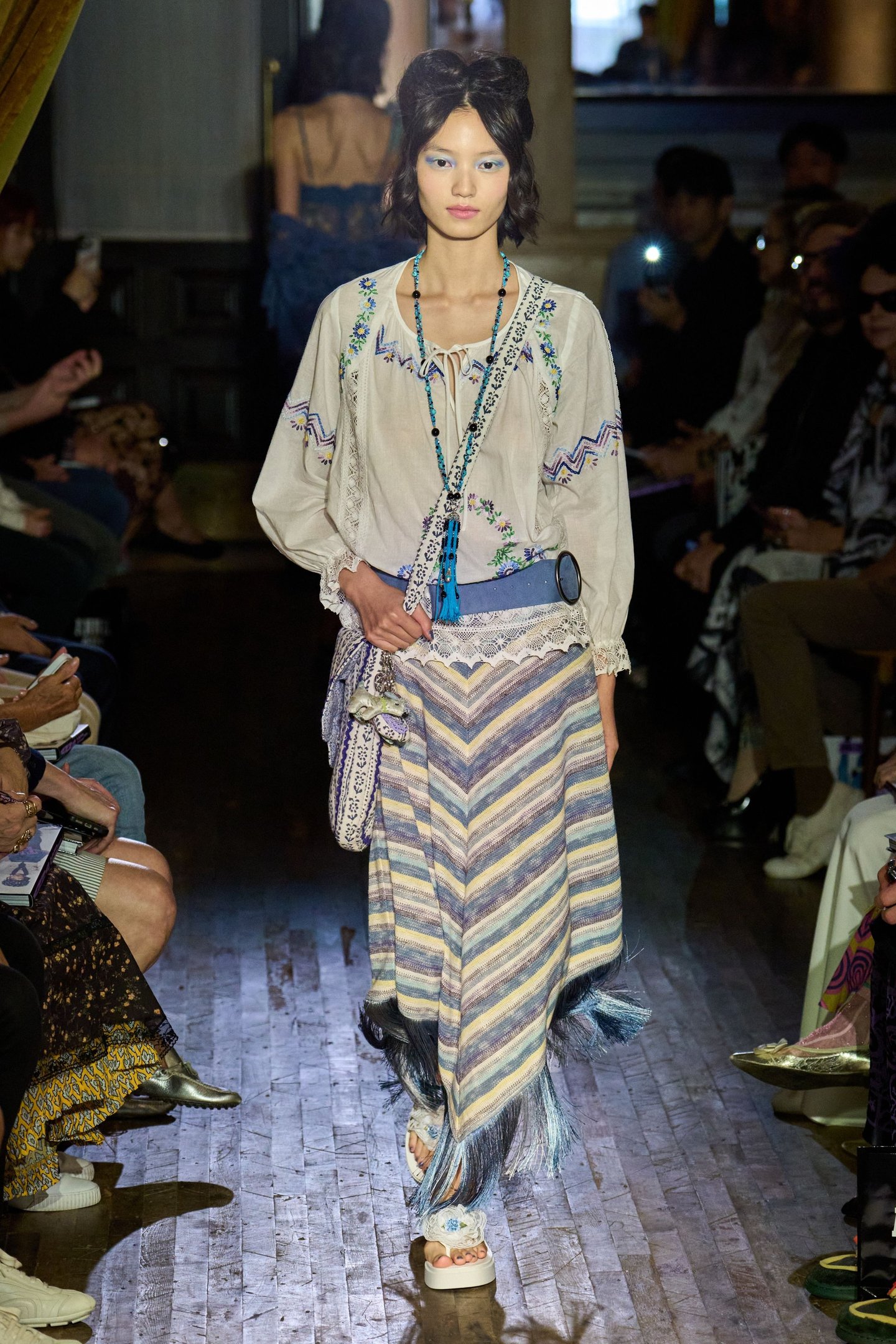 Modelo em passarela com traje boho chic listrado e adornos azuis na New York Fashion Week SS26.