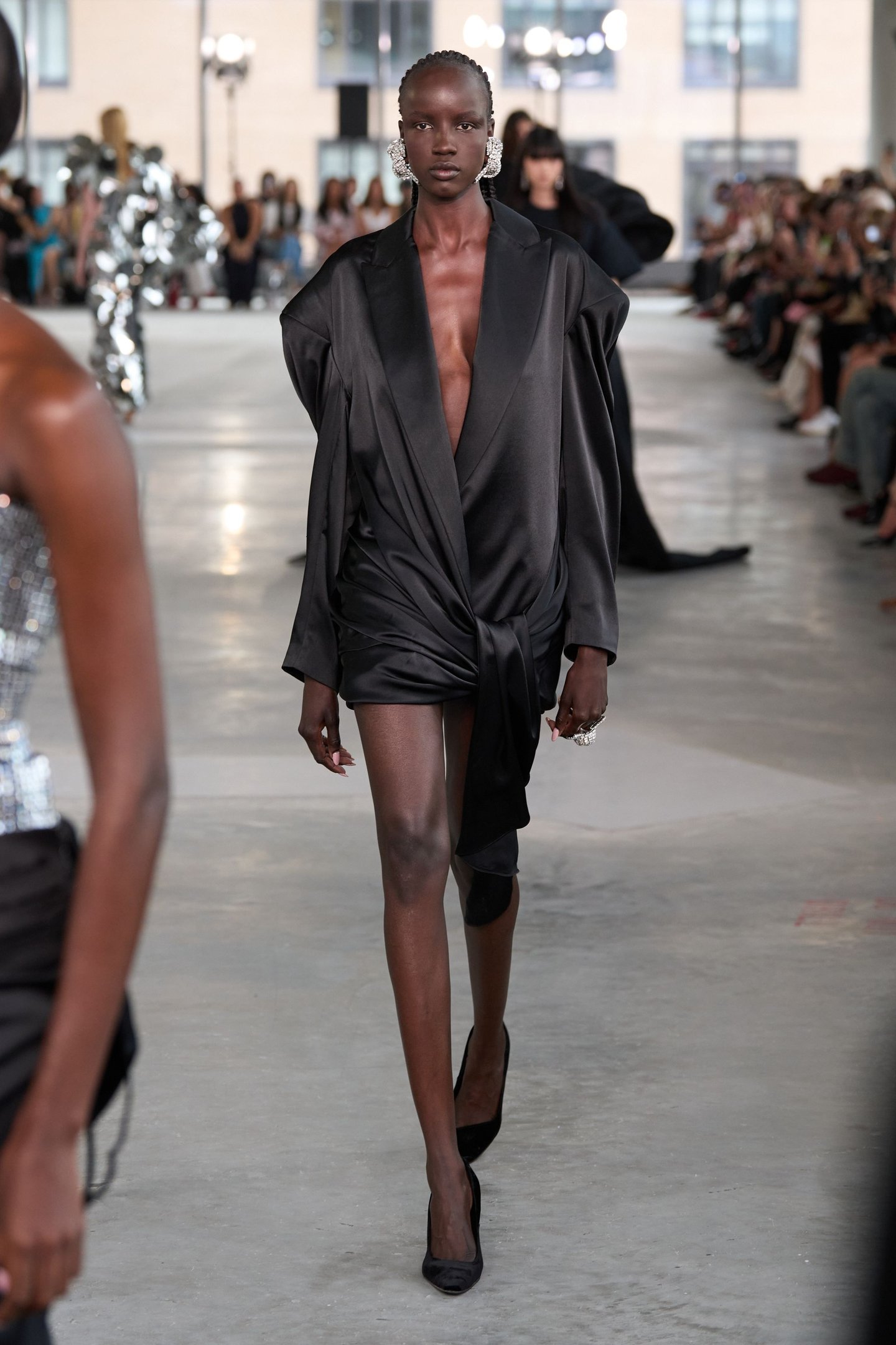 Modelo desfila com vestido preto drapeado e brincos prateados na New York Fashion Week SS26.