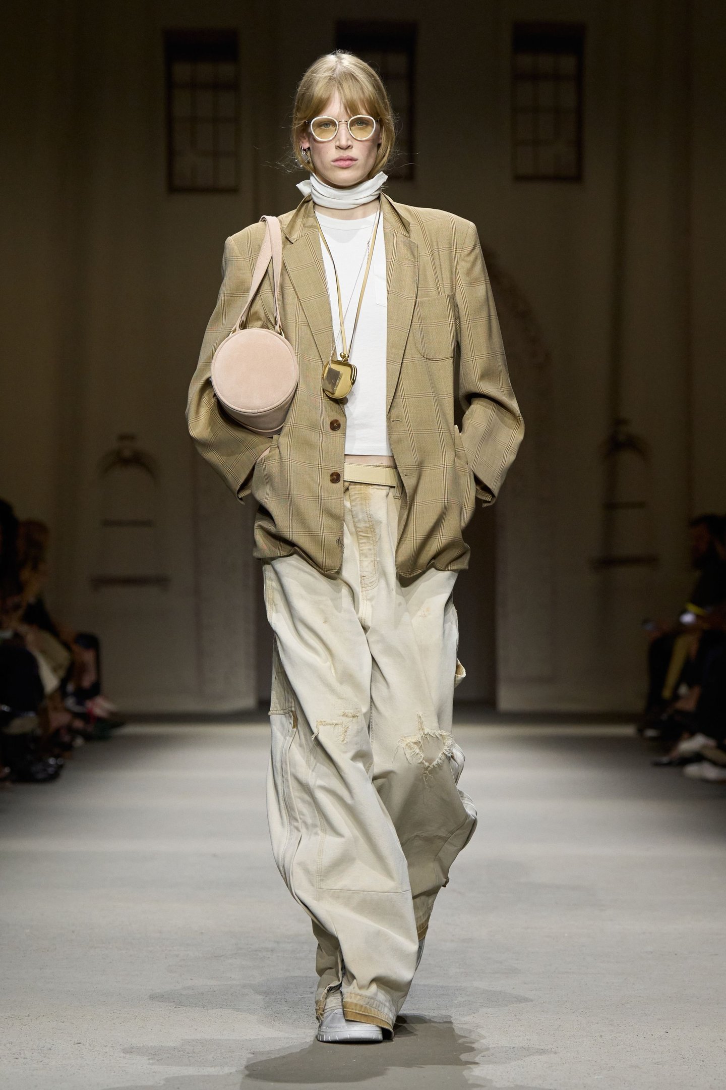 Modelo em passarela usa blazer xadrez, calças largas e bolsa redonda na New York Fashion Week SS26.