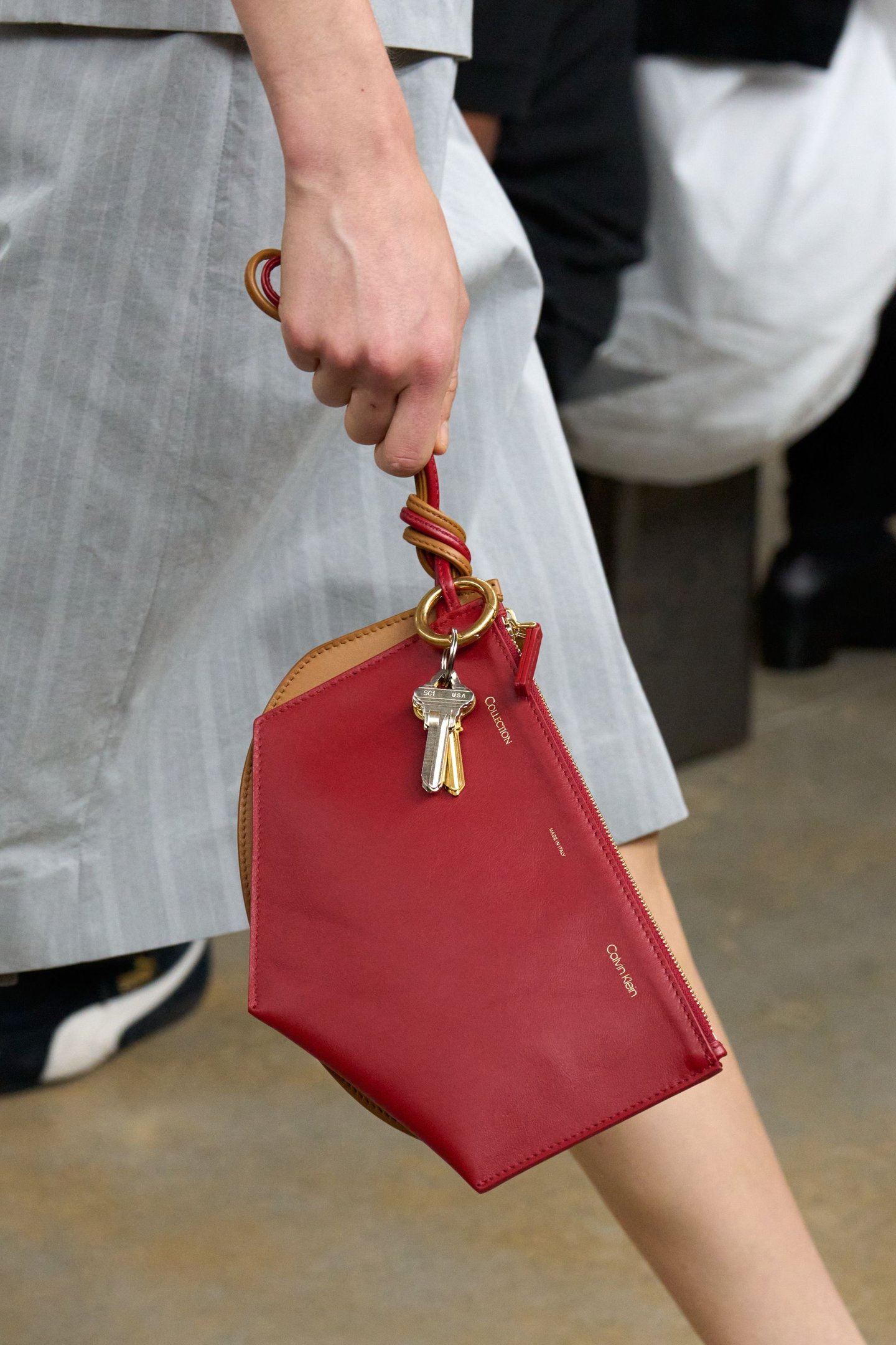 Bolsa vermelha da New York Fashion Week SS26, segurada por uma mão, com chaveiro dourado pendurado.