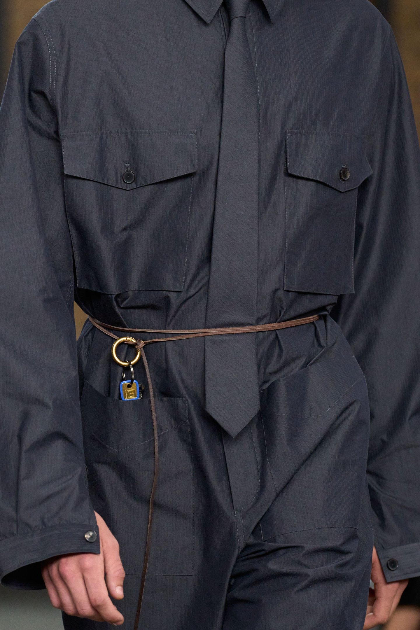 Desfile de modelo com roupa azul escura na New York Fashion Week SS26, destacando cinto marrom fino.