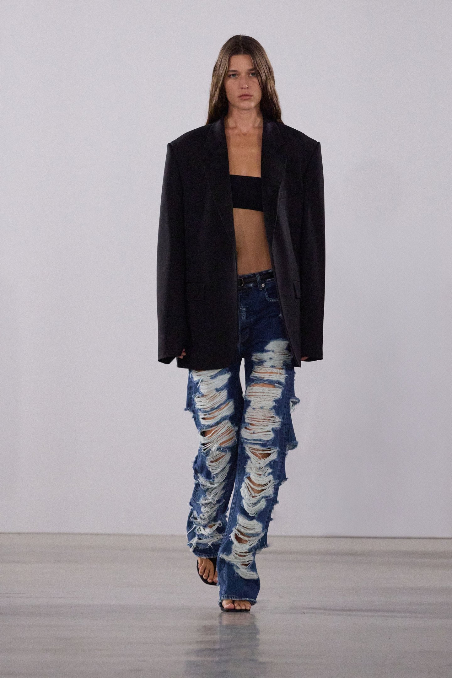 Modelo na passarela vestindo blazer preto, top preto e jeans rasgados durante a New York Fashion Week SS26.