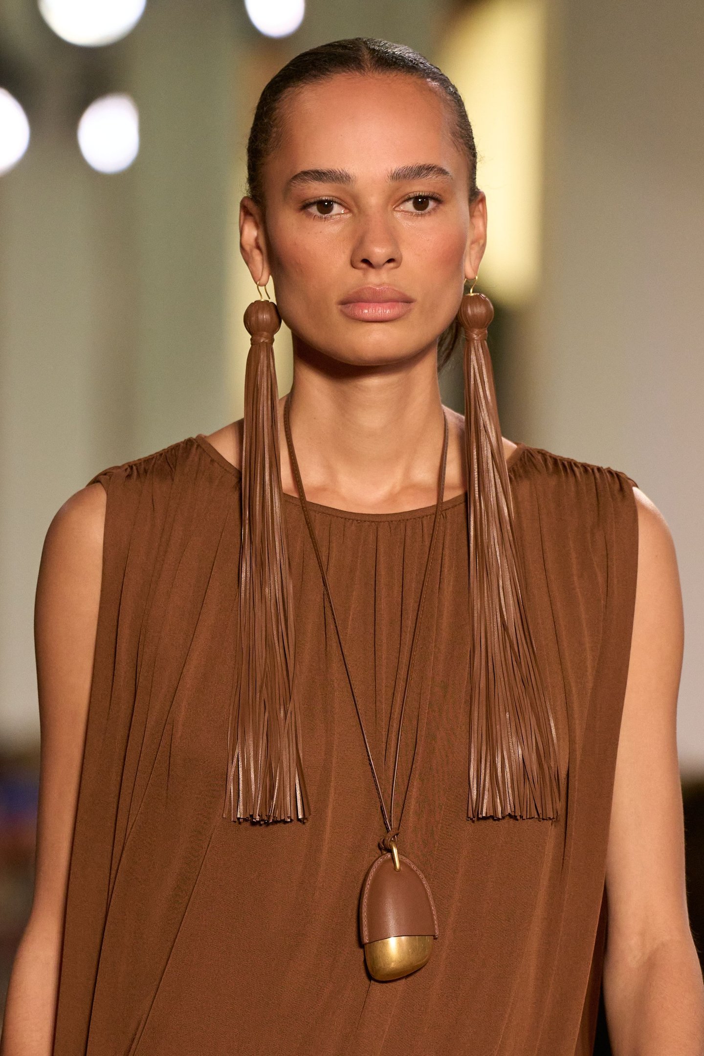 Modelo veste roupa marrom com brincos longos na New York Fashion Week SS26.