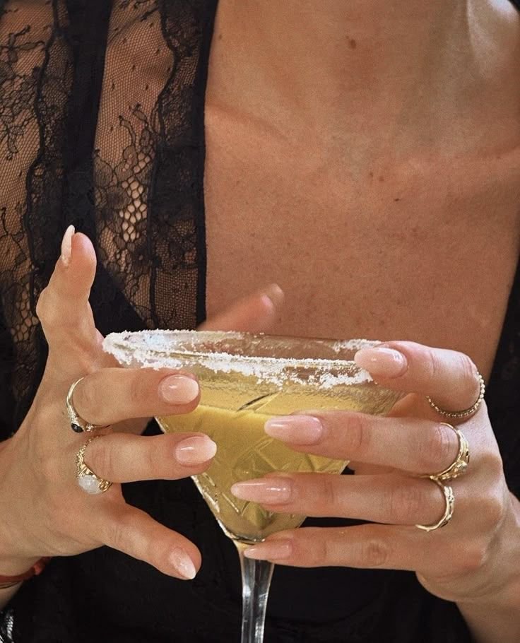 Taça de coquetel com borda de sal sendo segurada por mãos femininas com unhas bem feitas, ideal para festas.