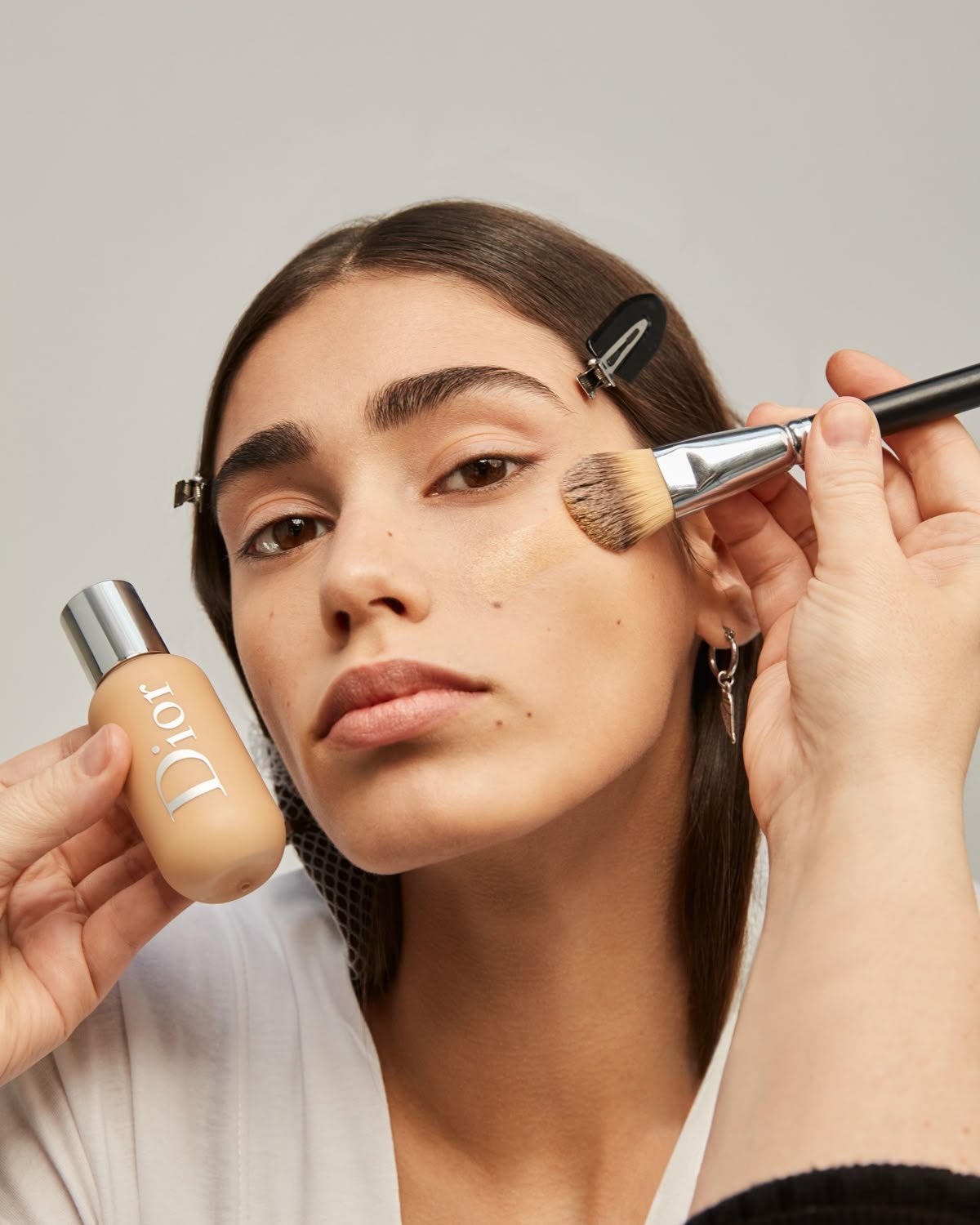 Mulher recebendo aplicação de base líquida com pincel de base, segurando produto.