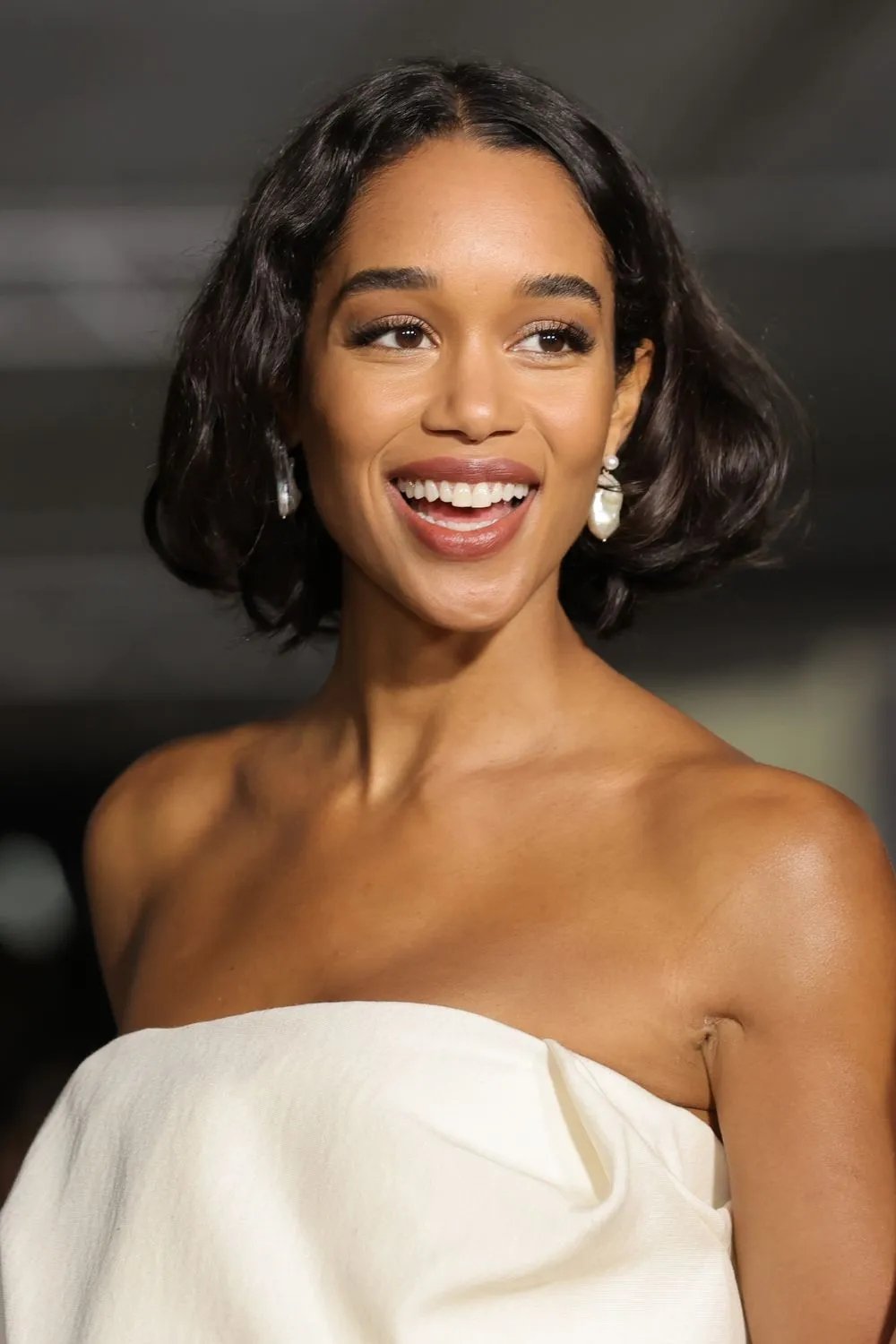 Mulher sorrindo usando cabelo estilo bob e vestido branco, com brinco pérola.