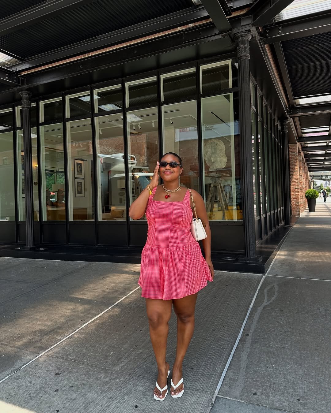 Pessoa em vestido vermelho vibrante, sorrindo e posando sob uma marquise perto de uma fachada envidraçada. Roupas coloridas