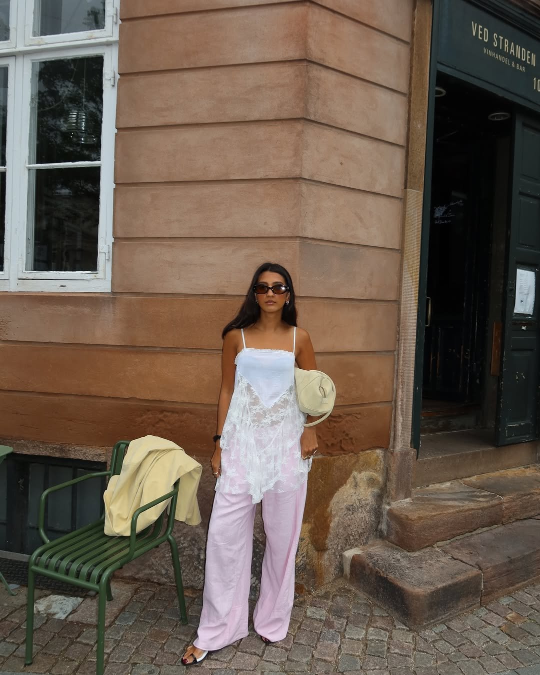 Pessoa com vestido branco rendado e calça rosa clara em frente a um prédio. Roupas coloridas