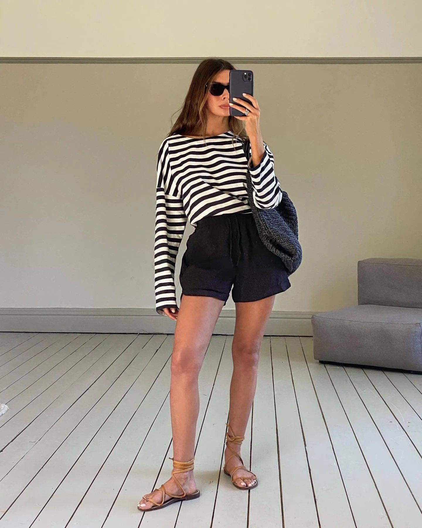 Listras preto e branco, shorts pretos e sandália de dedo tendência são usadas por mulher com óculos escuros, espelhando-se.